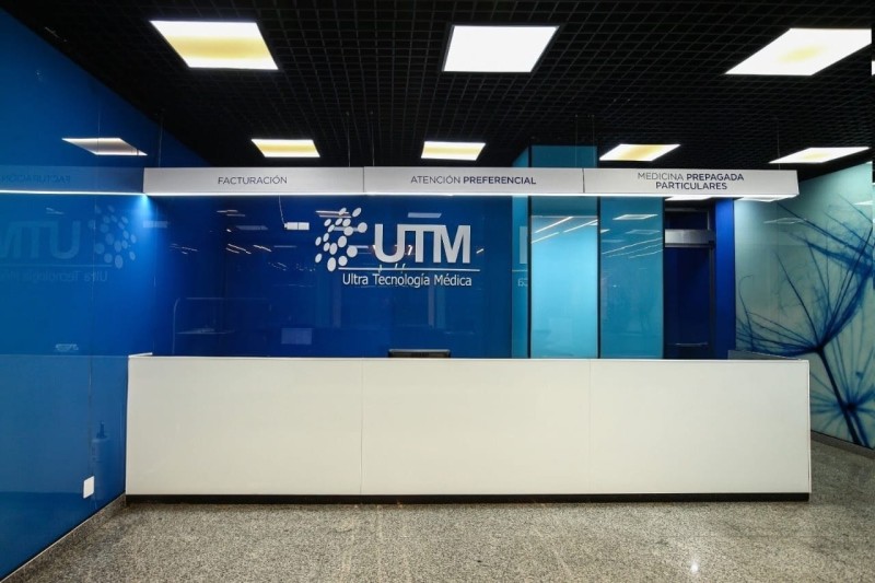 Recepción de UTM | Ultra Tecnología Médica con mostrador blanco y paredes de vidrio azul, señalando las áreas de facturación, atención preferencial y medicina prepagada o particulares.